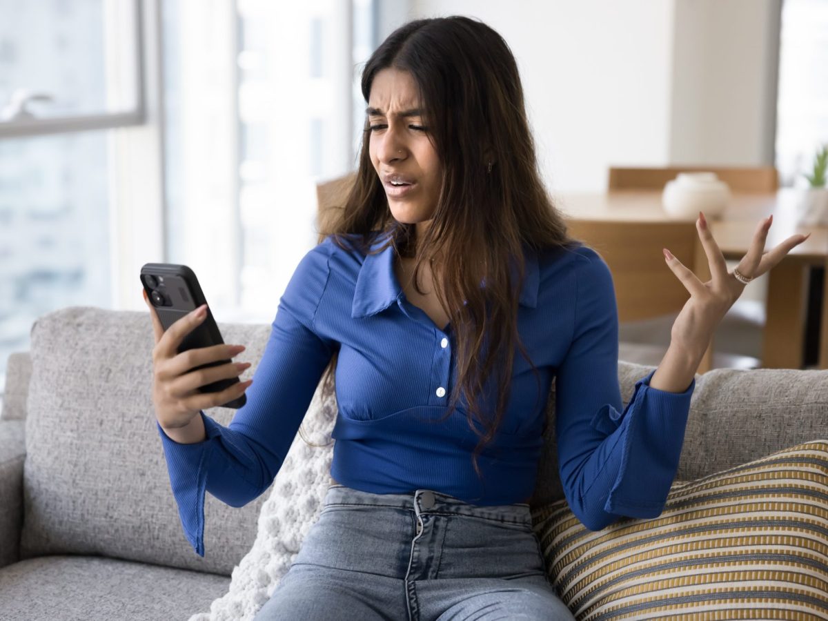 Frau hält Handy in der Hand und macht eine Geste der Unverständnis.