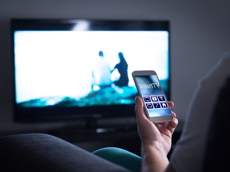 Person hält ein Smartphone vor einen Fernseher