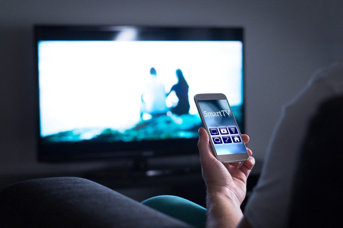 Person hält ein Smartphone vor einen Fernseher