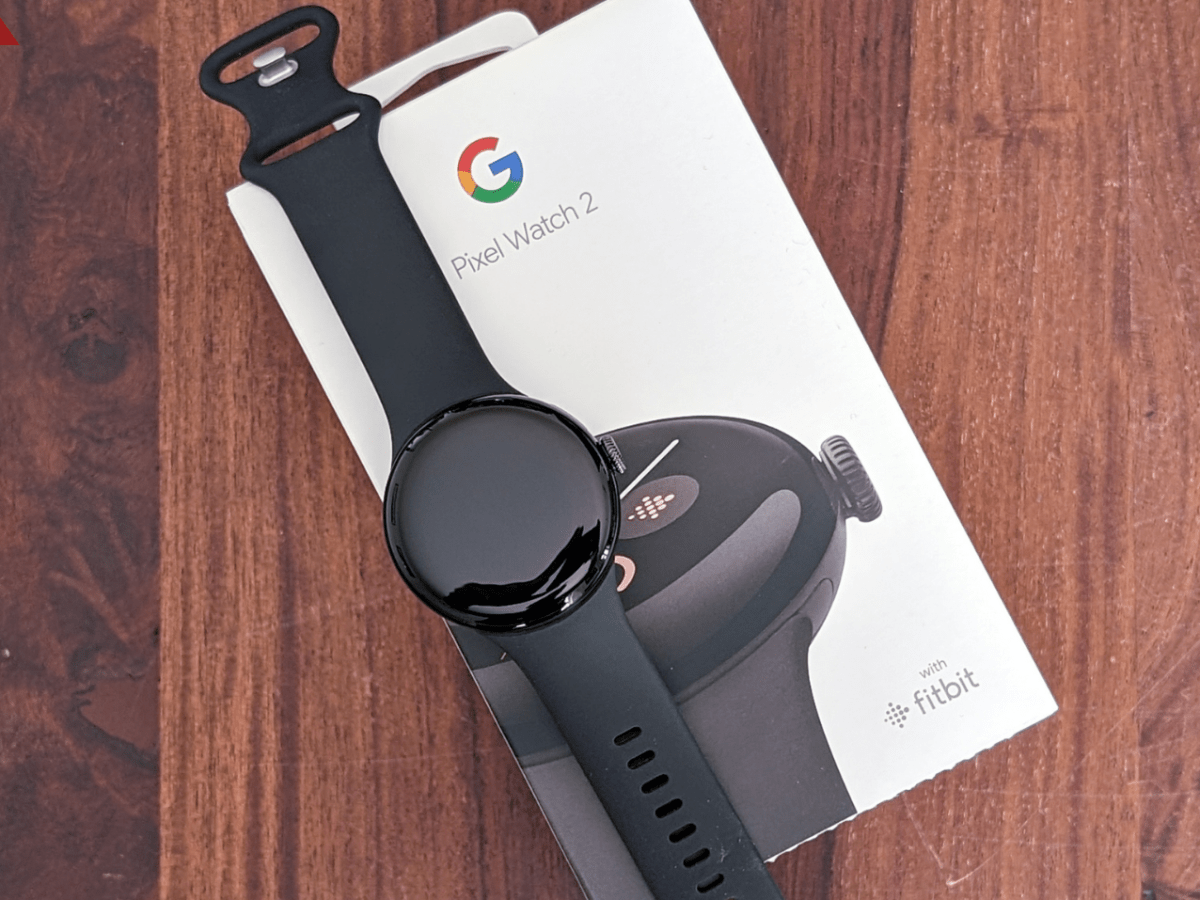 Google Pixel Watch 2 liegt auf einem Karton, der auf einer Unterlage aus Holz liegt,