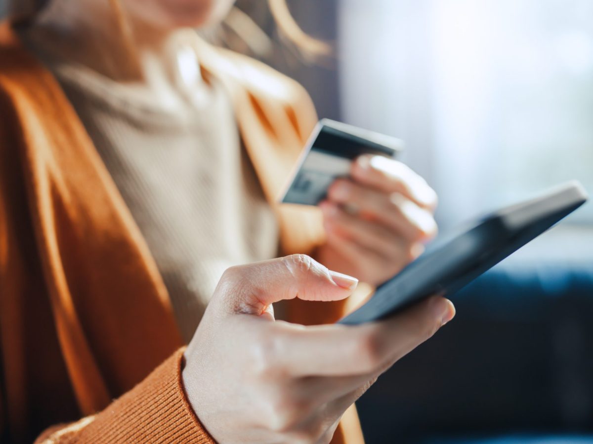 Eine Person hält in der einen Hand ein Handy und in der anderen Hand eine Bankkarte