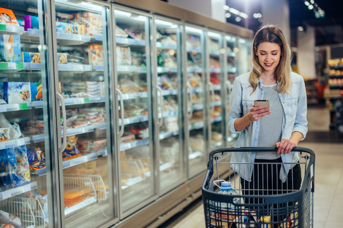 Frau steht im Supermarkt und blickt auf ihr Handy.