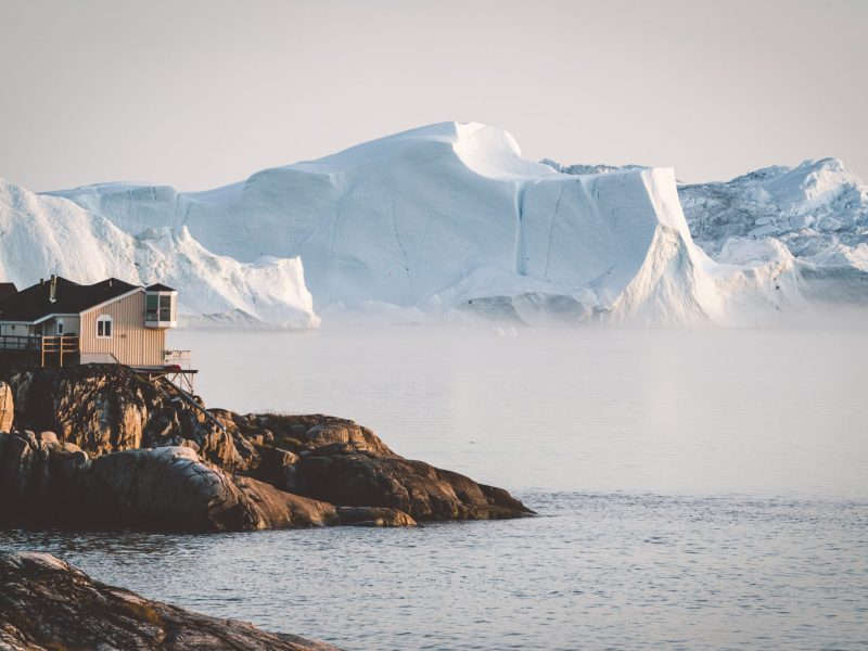 Eine HolzhÃ¼tte steht an einer FelskÃ¼ste. Im Hintergrund ist eine riesige Eisformation zu sehen.