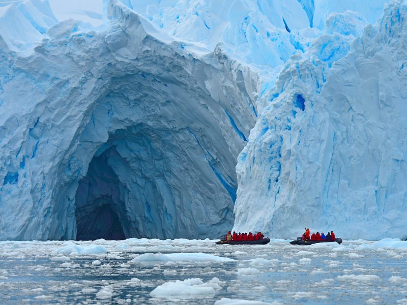 Zwei Boote mit zahlreichen Passagieren stehen vor der Ã–ffnung einer riesigen HÃ¶hle in einem Gletscher.