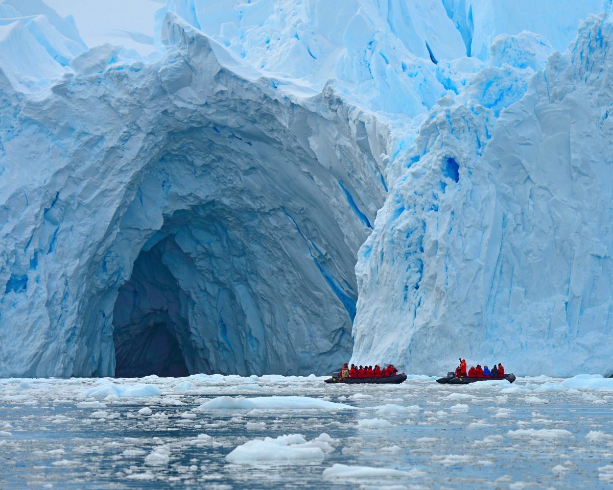 Zwei Boote mit zahlreichen Passagieren stehen vor der Ã–ffnung einer riesigen HÃ¶hle in einem Gletscher.