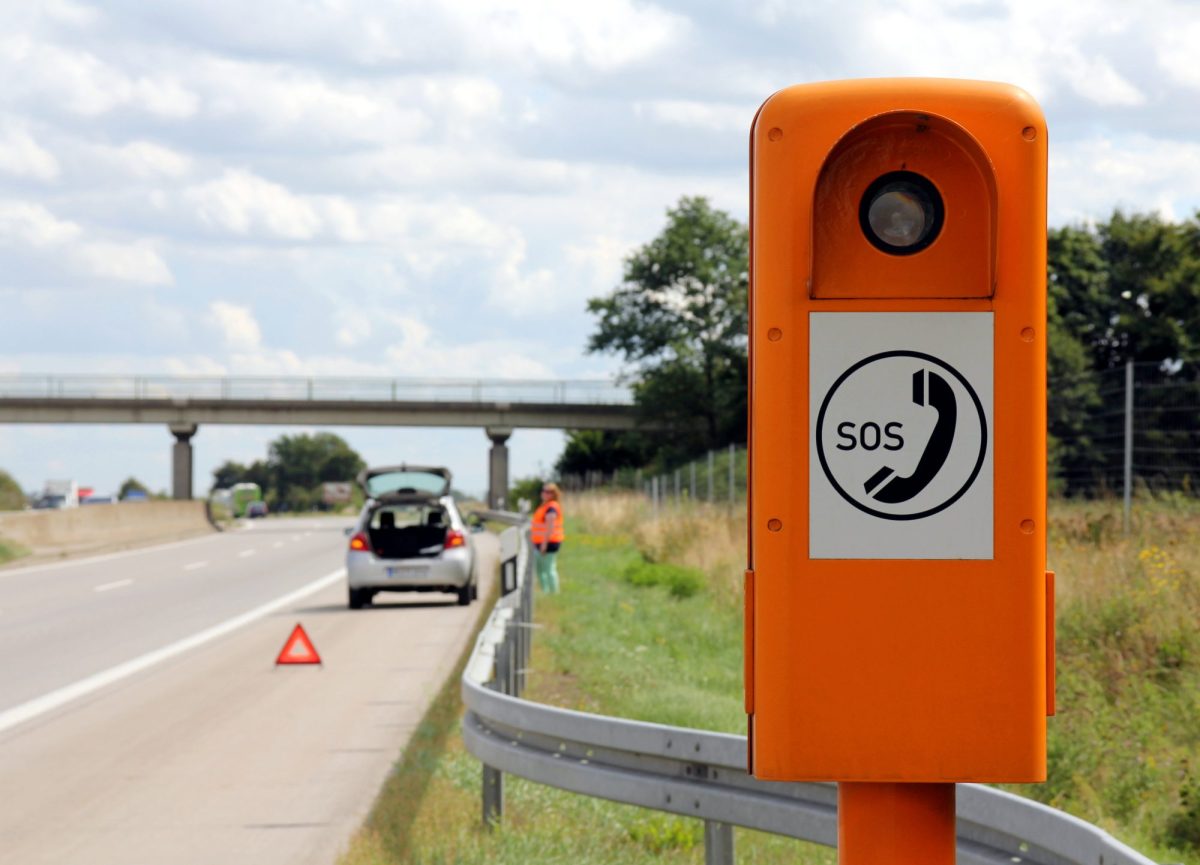 SOS-SÃ¤ule an einer Autobahn. Im Hintergrund ist ein Auto zu sehen, das hinter einem Warndreieck auf dem Seitenstreifen steht.