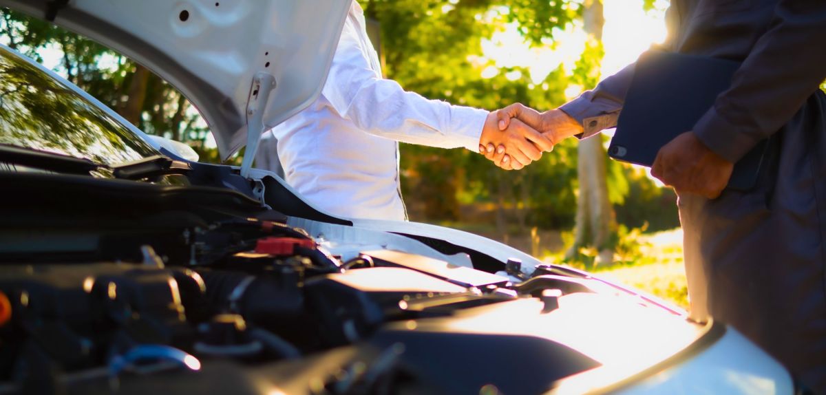 Auto mit offener Motorhaube vor zwei Personen, die sich die Hand schÃ¼tteln