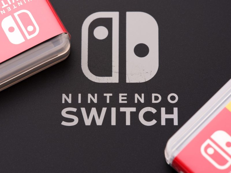 Nintendo Switch-Logo auf dunklem Untergrund. Daneben liegen zwei Nintendo Switch-Spiele.