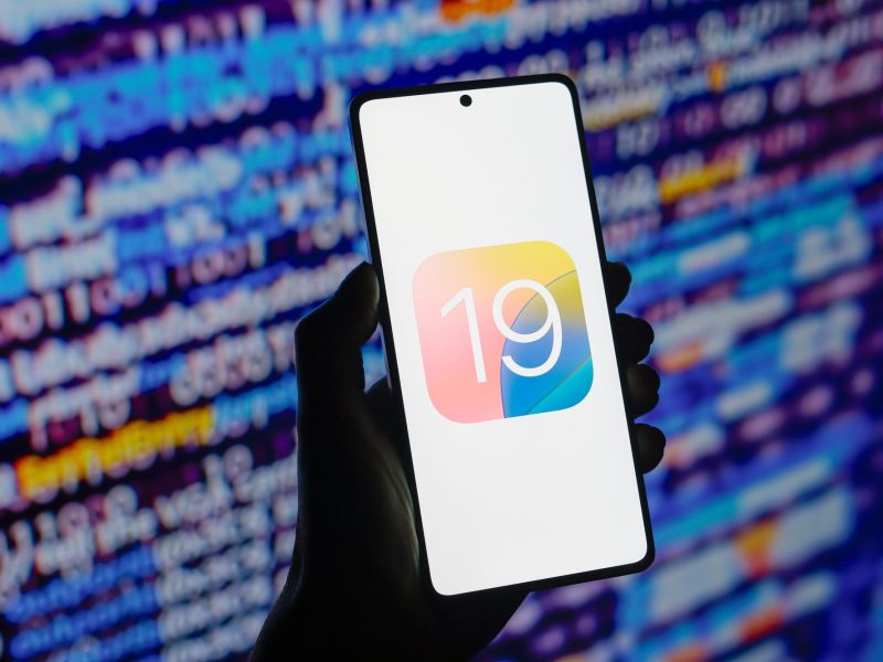 Person hÃ¤lt Smartphone in der Hand. Auf dem Bildschirm das Logo von iOS 19.