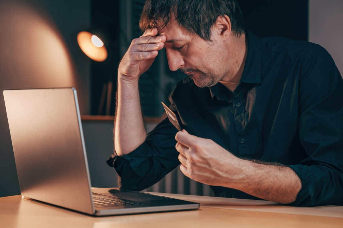 Mann hÃ¤lt verzweifelt die Hand an den Kopf, wÃ¤hrend er vor einem Laptop sitzt, mit einer Bankkarte in der Hand