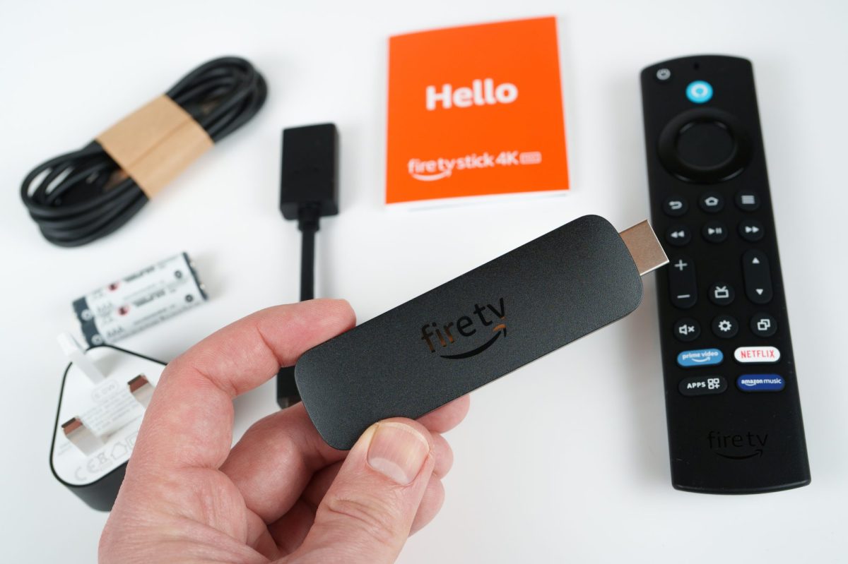 Person hÃ¤lt einen Amazon Fire TV-Stick. IM Hintergrund liegt das entsprechende ZubehÃ¶r.