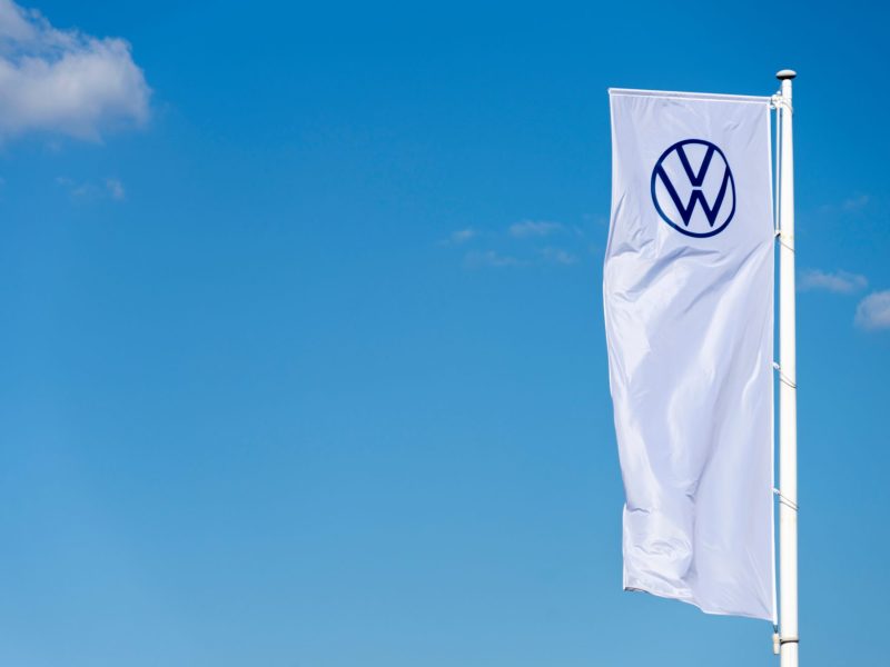 WeiÃŸe Fahne mit VW-Logo vor blauem Himmel.