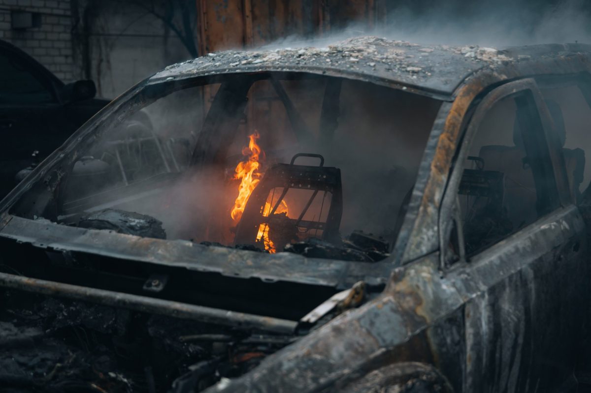 Ausgebranntes Auto. Im Inneren lodert noch eine Flamme.